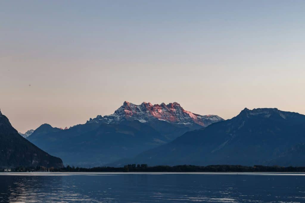 Dent du midi vue du Léman, légèrement éclairée par un rayon de soleil doux avec le lac Léman calme au premier plan qui forme un miroir d'eau.